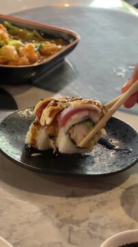 Hand lifting a sushi roll with chopsticks and soy sauce