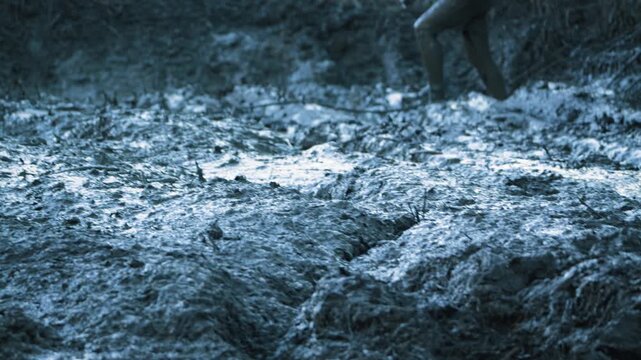 An SUV is stuck in deep, wet mud. The co-pilot tries to push it out. A close-up shot from a low angle focuses on the thick mud. The cool blue color tone creates a tense, adventurous atmosphere