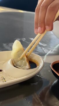 Gyoza dumpling dipped into soy sauce with chopsticks