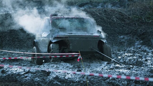 Action shot of powerful 4x4 vehicle struggling in muddy terrain. Steam billows from engine as truck is pulled by winch. Gritty, intense scene from off-road rally with cool, muted colors