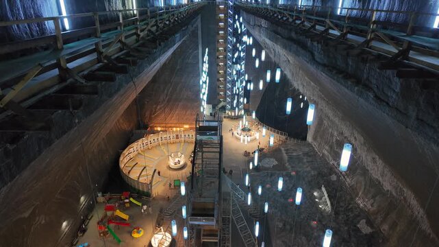 Massive underground salt mine cavern with towering wooden structures and glowing lights, seen in a dramatic tilt up view from below