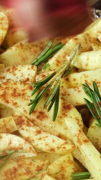 Vertical video. Preparing potatoes for baking. Hand sprinkling paprika spices onto slices of raw potatoes with rosemary