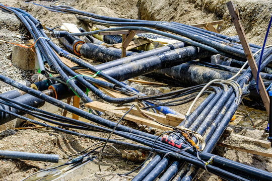 Construction site shows a large hole with exposed pipeline located in an urban area during daylight hours with equipment nearby
