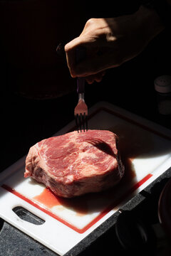 Hand holding fork over raw cupim beef on cutting board
