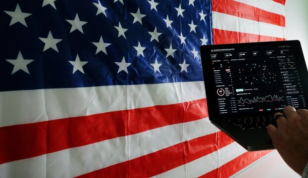 Man working on laptop displaying surveillance tracking dashboard in front of American flag, representing digital privacy and Fourth Amendment rights