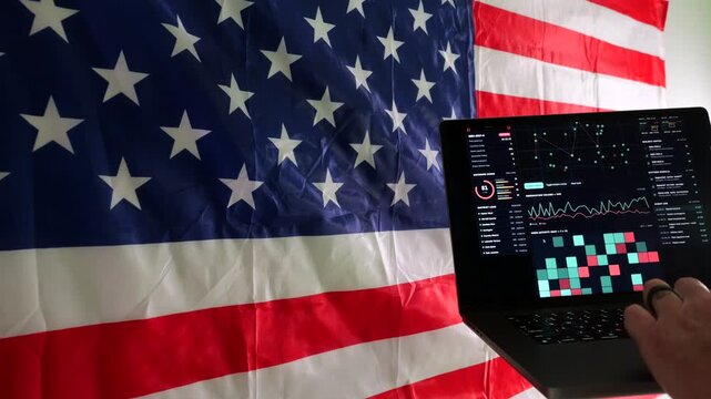 Man working on laptop displaying surveillance tracking dashboard in front of American flag, representing digital privacy and Fourth Amendment rights