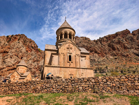 View of Noravank monastery with its distinctive stone architecture set against dramatic red cliffs and a clear blue sky in Areni, Vayots Dzor Province, Armenia.