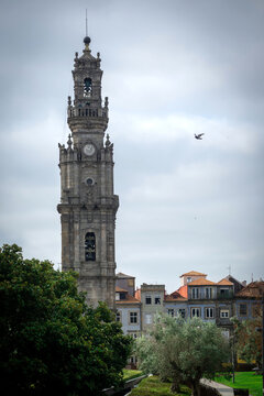 View of the historic Torre dos Clerigos bell tower rising above traditional buildings with tiled facades under a cloudy sky in Porto, Porto, Portugal.