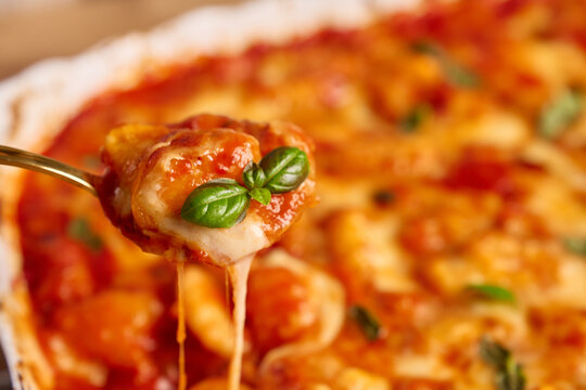 Gnocchi with tomato sauce, melted mozzarella and basil served on spoon above baking dish