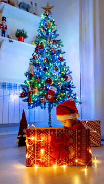 Child in Santa hat sitting in a festive gift box at home