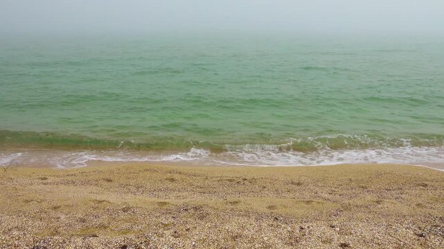 Pearl fog, green sea and yellow sand on a morning day with weak surf. Sea of Azov