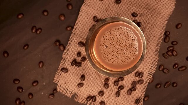 A traditional south indian Brass cup of coffee over beans background