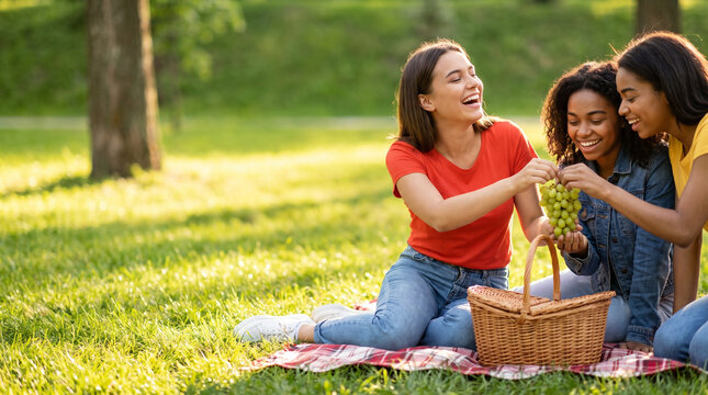 Three friends enjoying a picnic with grapes on a sunny park grass  