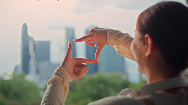 Back view close up hands of Asian woman making frame gesture looking at city skyline during sunset, visionary female planning future goals for business strategy, perspective, creative inspiration