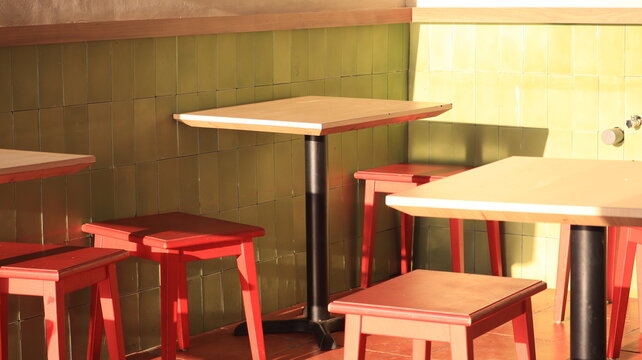 Minimalist restaurant interior with red wooden stools and green tiled wall under natural sunlight