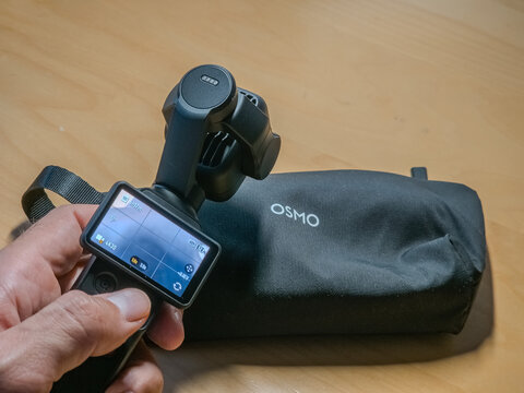 Barcelona, Spain. August 03, 2026, Hand holding the DJI Osmo Pocket 4P or 4 pro, a compact 4K camera and gimbal, with its carrying case on a wooden surface