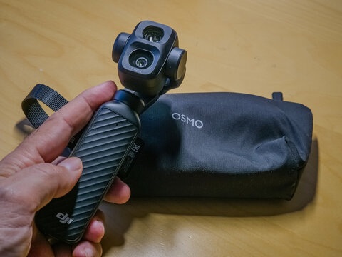 Barcelona, Spain. August 03, 2026, Hand holding DJI Osmo Pocket 4P or 4 pro, a compact gimbal camera for stable video recording, with its carrying case on a wooden surface
