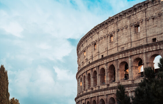 Colosseum, an iconic ancient Roman amphitheater, stands against a bright blue sky filled with white clouds, showcasing its historic architecture and enduring legacy as a symbol of the Roman Empire