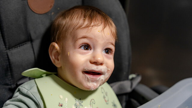 Smiling baby in high chair with messy face after meal