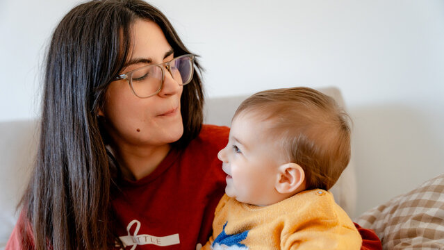 Mother with eyeglasses cuddling baby on sofa at home