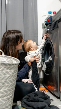 Mother helping baby explore laundry room by washing machine
