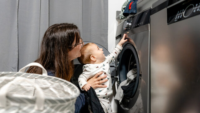 Mother helps baby press buttons on front-loading washer
