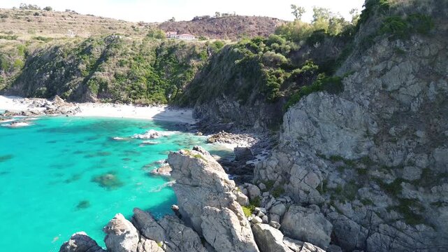Zambrone, Calabria, Italy. Lateral aerial drone flight along rugged coastal cliffs and a secluded pebble cove with crystal-clear turquoise Tyrrhenian water on the Costa degli Dei.