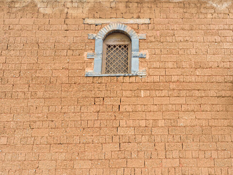 Arched window with stone framing on textured traditional mud brick wall