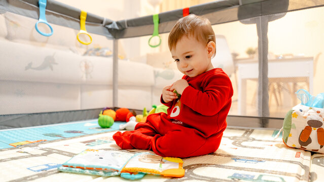 Baby sitting in playpen with toys and soft book at home