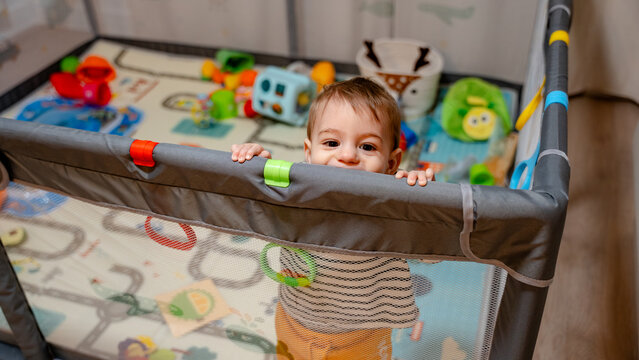 Toddler peeking over playpen in colorful indoor nursery