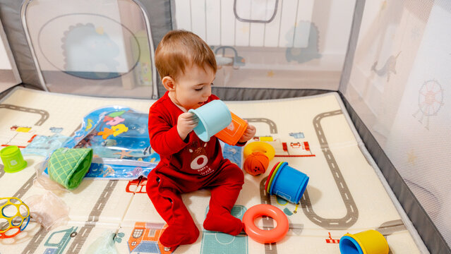 Toddler playing with colorful stacking cups in playpen