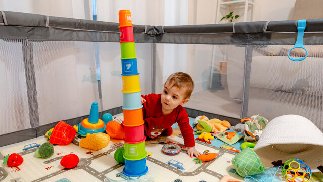 Toddler playing with colorful stacking cups in playpen