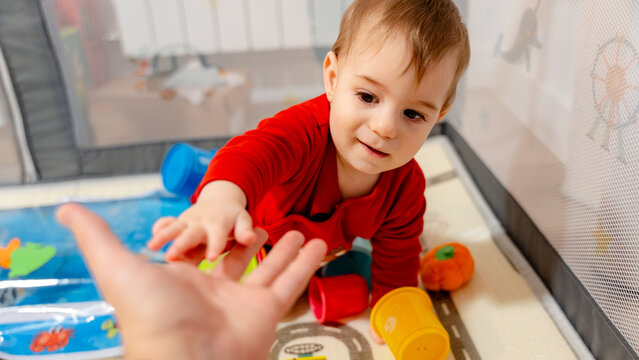 Toddler reaching for parent's hand in indoor playpen