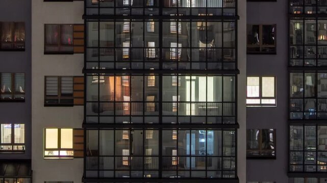 facade of a modern apartment building at night, lights on in the windows, panorama down