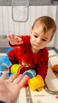 Toddler reaching for parent hand while playing with cups