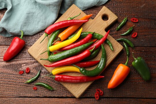Fresh colorful chili peppers on wooden table, flat lay