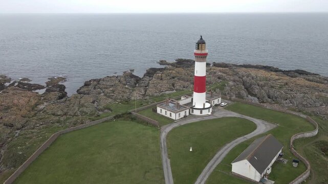 Tracking over Buchan Ness Lighthouse towards the sea. Located on the rugged North Sea coast at Boddam near Peterhead, Aberdeenshire, Scotland. The iconic red and white lighthouse stands on a rocky hea