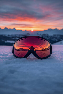 Ski goggles on fresh snow reflecting mountain sunset