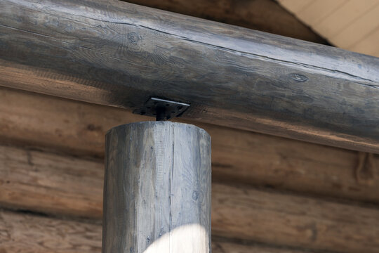 Close-up view of a rustic log cabin timber post supporting a horizontal beam, highlighting natural wood grain, joinery details and a metal plate fastener in warm, weathered architectural texture