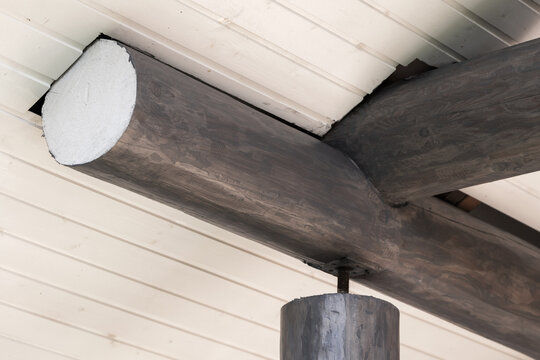 Rustic interior detail showing a close-up of a wood beam ceiling with a timber support post and exposed log joint. Neutral tones highlight wood grain, texture, construction and architectural detail