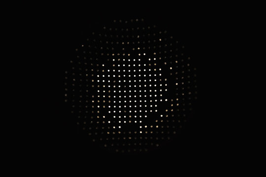 Soft warm light shining through a perforated circular surface creates a dotted matrix and minimalist abstract pattern on a black background, suggesting modern design, mystery and subtle texture