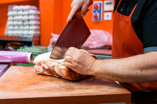 Butcher cutting meat with cleaver on chopping block