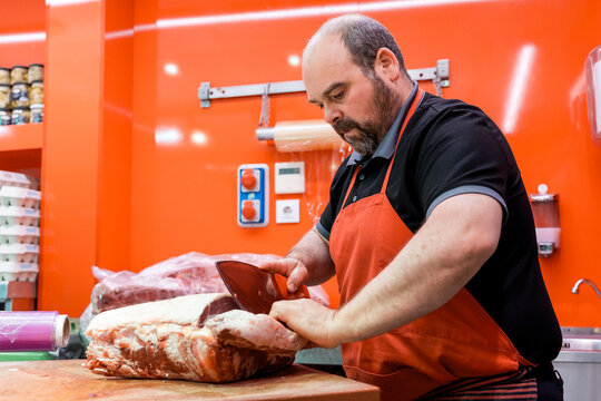 Butcher slicing fresh meat with cleaver on wooden board