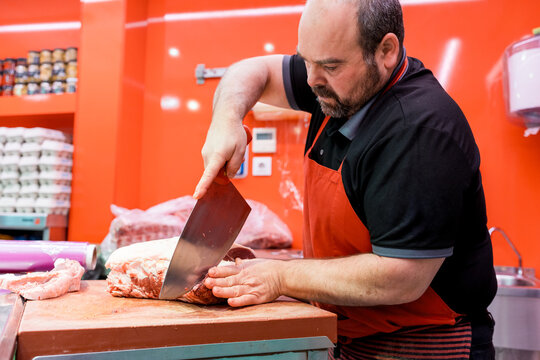 Butcher cutting fresh meat with cleaver on shop counter