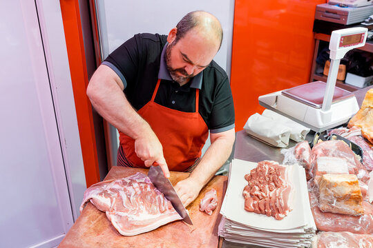 Butcher trimming meat at counter in traditional meat shop