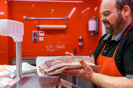 Butcher weighing fresh meat belly on scale in meat shop
