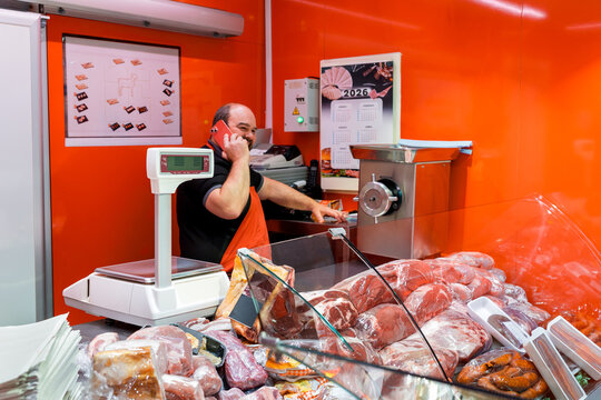 Butcher talking on phone behind meat counter in shop