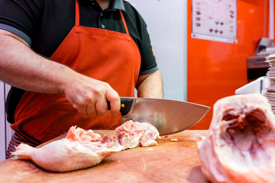 Butcher cutting raw meat with cleaver on wooden block