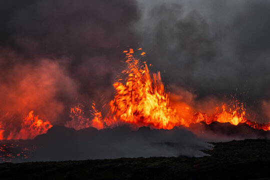 View of a powerful volcanic eruption with glowing lava fountains and thick smoke rising into the dark sky in Iceland.