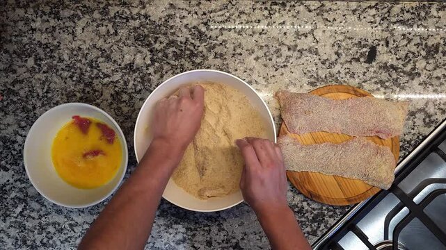 Manos empanando milanesas de carne con huevo y pan rallado